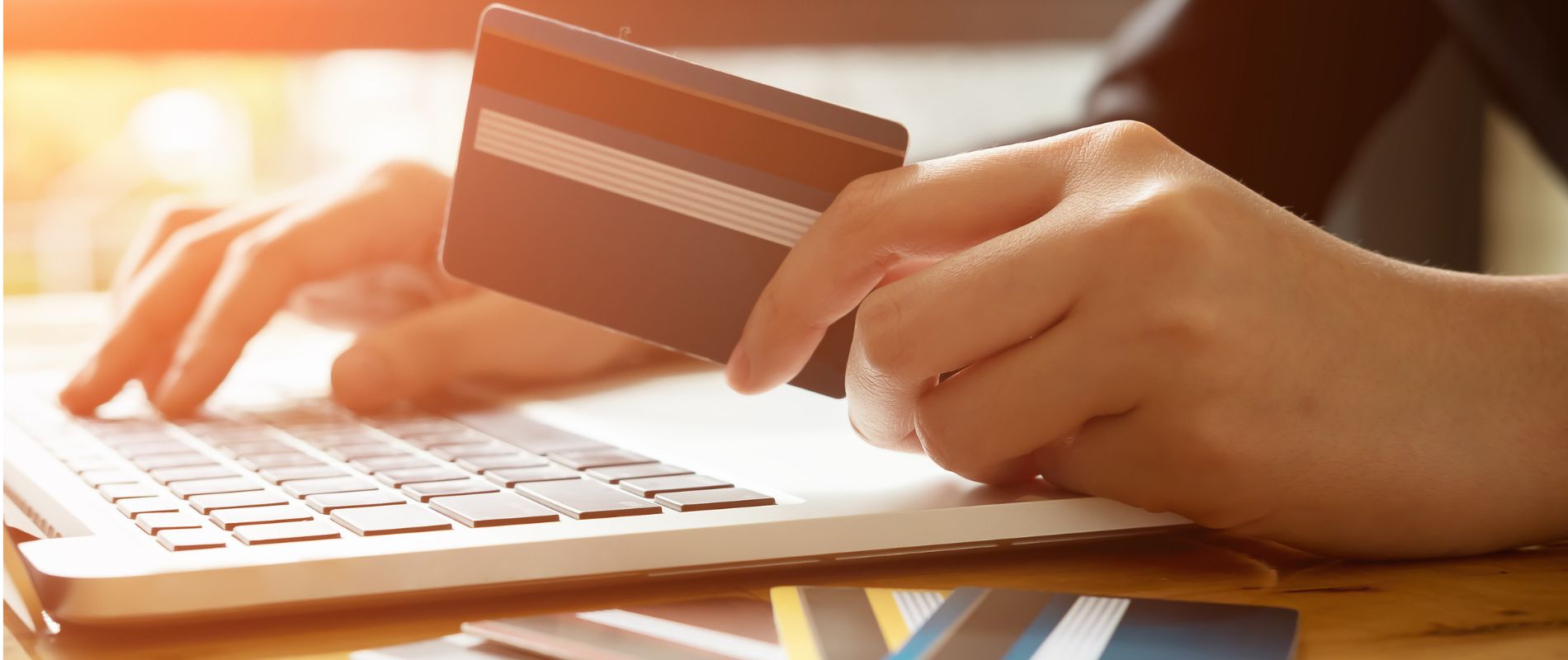 close up of hands, one holding a credit card, the other typing on a pc.