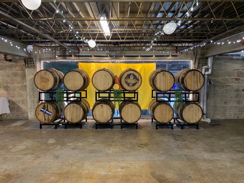 Stacked wooden beer barrels with plants and a yellow New Mexico flag backdrop, decorated with string lights and balloons.