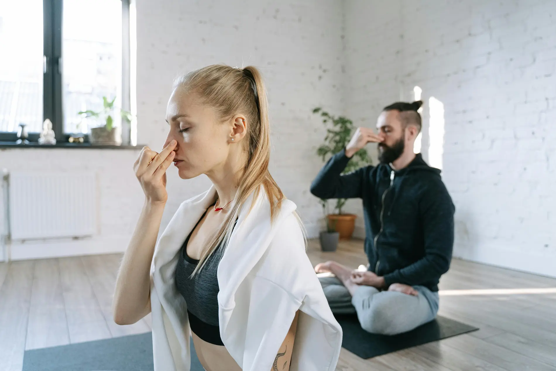 A man and a woman sitting cross-legged while practicing alternate nostril breathing.
