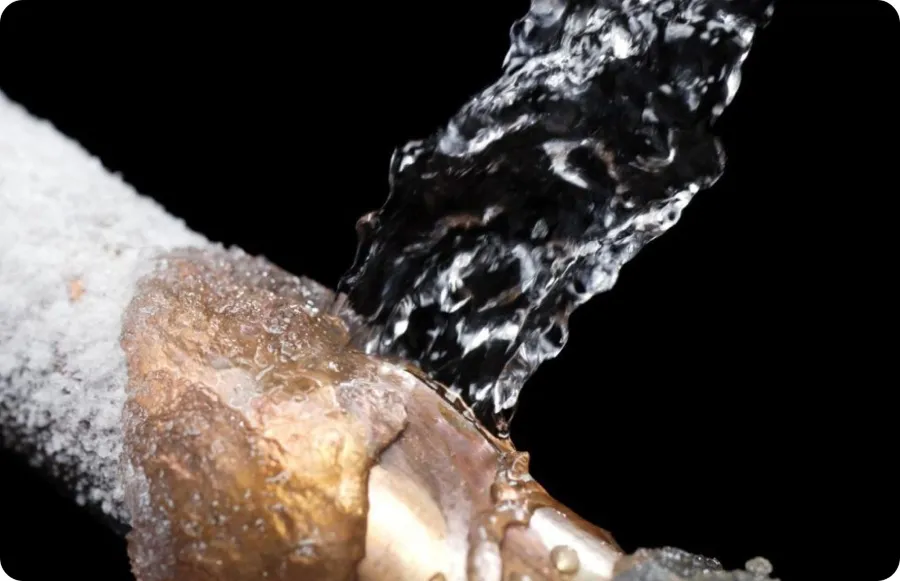 Close-up of a burst frozen pipe spraying water under pressure