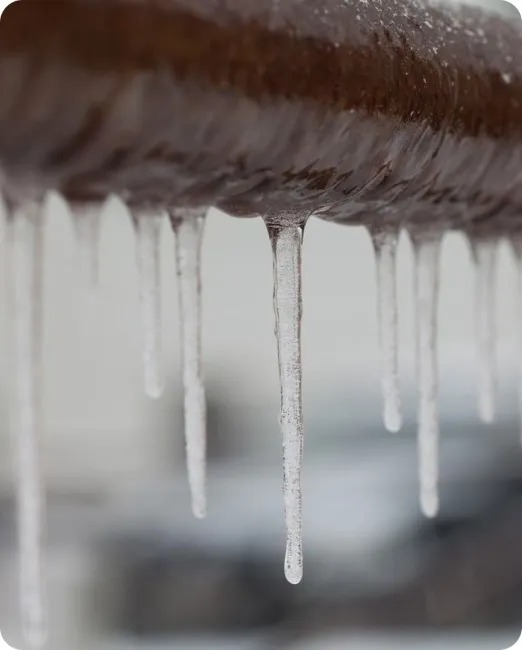 Close-up of a frozen metal pipe with hanging icicles showing winter freeze prevention example
