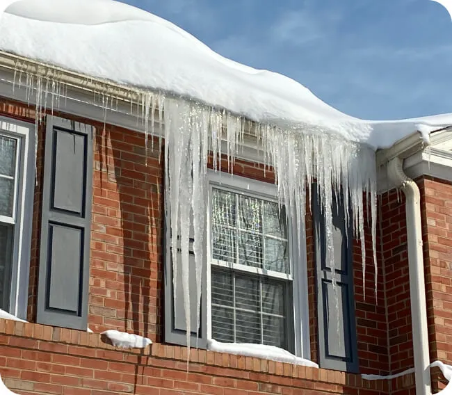 Icicles and ice dams forming along the roof edge of a brick house in winte