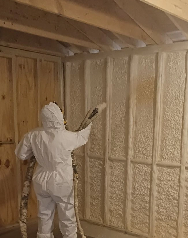 Technician in protective suit spraying foam insulation into framed interior wall cavities
