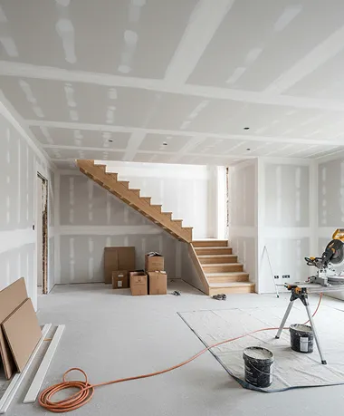 Interior home remodeling scene with new drywall installation, unfinished staircase, and construction tools in a bright open room