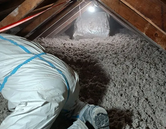 Technician installing cellulose insulation in an attic, showing fire-resistant loose-fill material between wooden rafters.