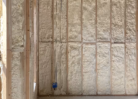 Closed-cell spray foam insulation applied inside 2x4 wall framing, showing a fully insulated exterior wall cavity