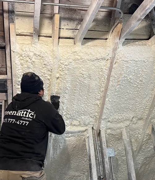 Green Attic technician trimming excess closed cell spray foam insulation from wall cavities