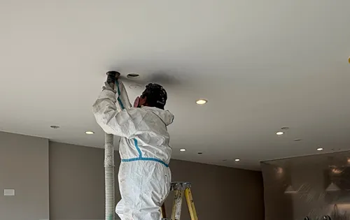 Technician installing blown-in insulation through a conventional ceiling access hole to improve attic thermal performance