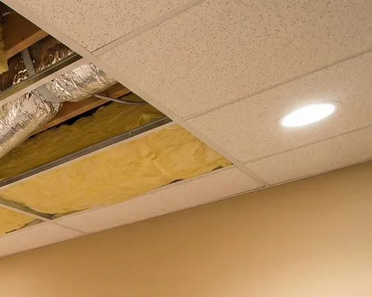 Suspended ceiling with tiles removed to show fiberglass insulation batts and ductwork above