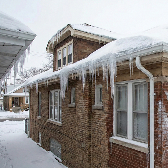 Brick bungalow with severe roof ice dams and long icicles caused by poor attic insulation and heat loss