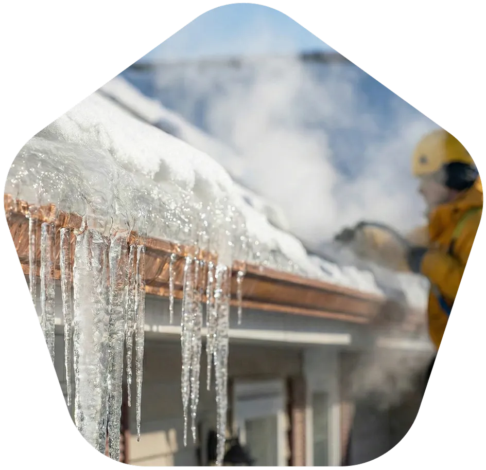 Worker performing ice dam removal with steam on snowy roof