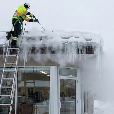 Technician performing ice dam removal with steam on a commercial storefront roof.