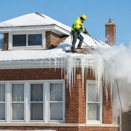 Worker performing ice dam removal with steam on a brick home roof