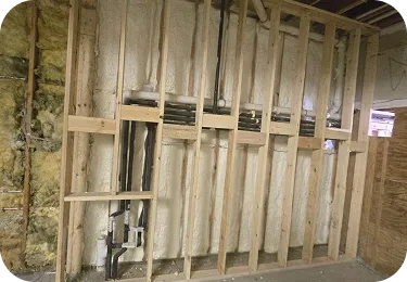 Completed spray foam insulation on a basement utility wall behind wooden framing.