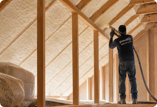 Spray foam insulation being installed in an attic between roof rafters.