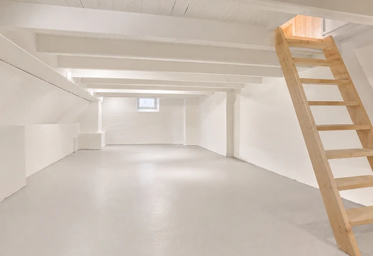 Clean finished basement storage area with white walls, smooth floor, and wooden access ladder.