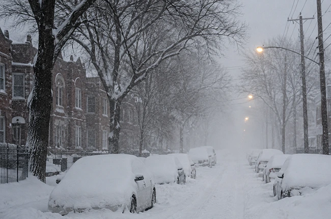 Chicago street during heavy snowfall with parked cars covered in snow.