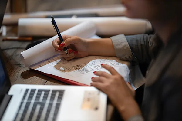 Personne dessinant des plans techniques à la main à côté d'un ordinateur portable