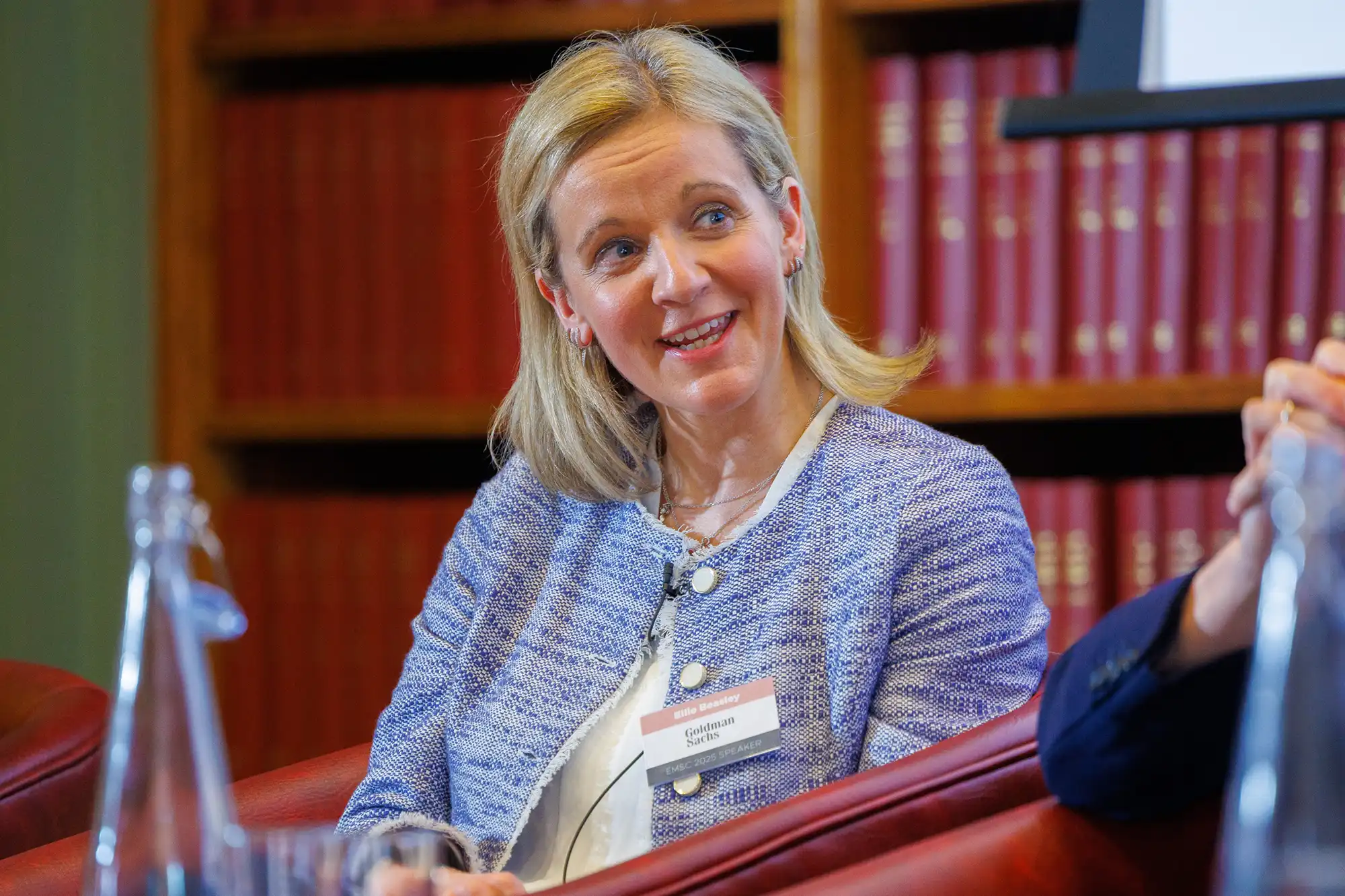 Ellie Beasley from Goldman Sachs smiles during a panel discussion at the EMSC 2025 conference. She is wearing a blue and white patterned tweed jacket.