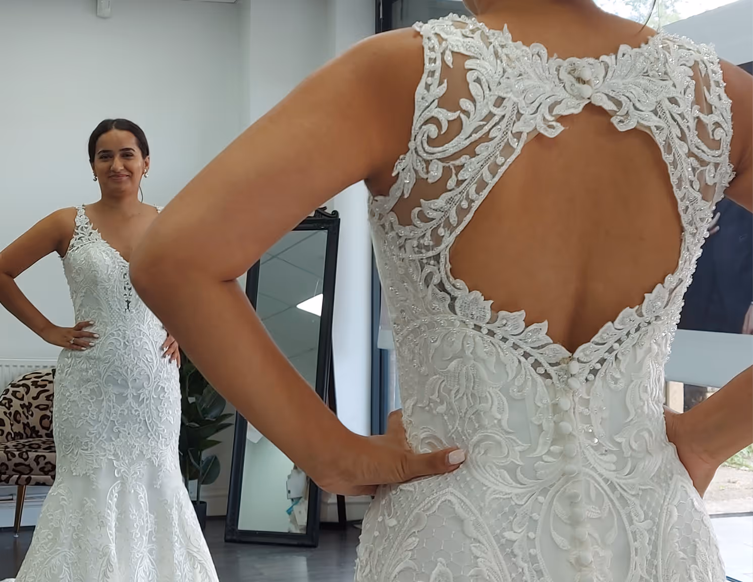 Woman trying on a white lace wedding dress with a keyhole back detail in front of a mirror.