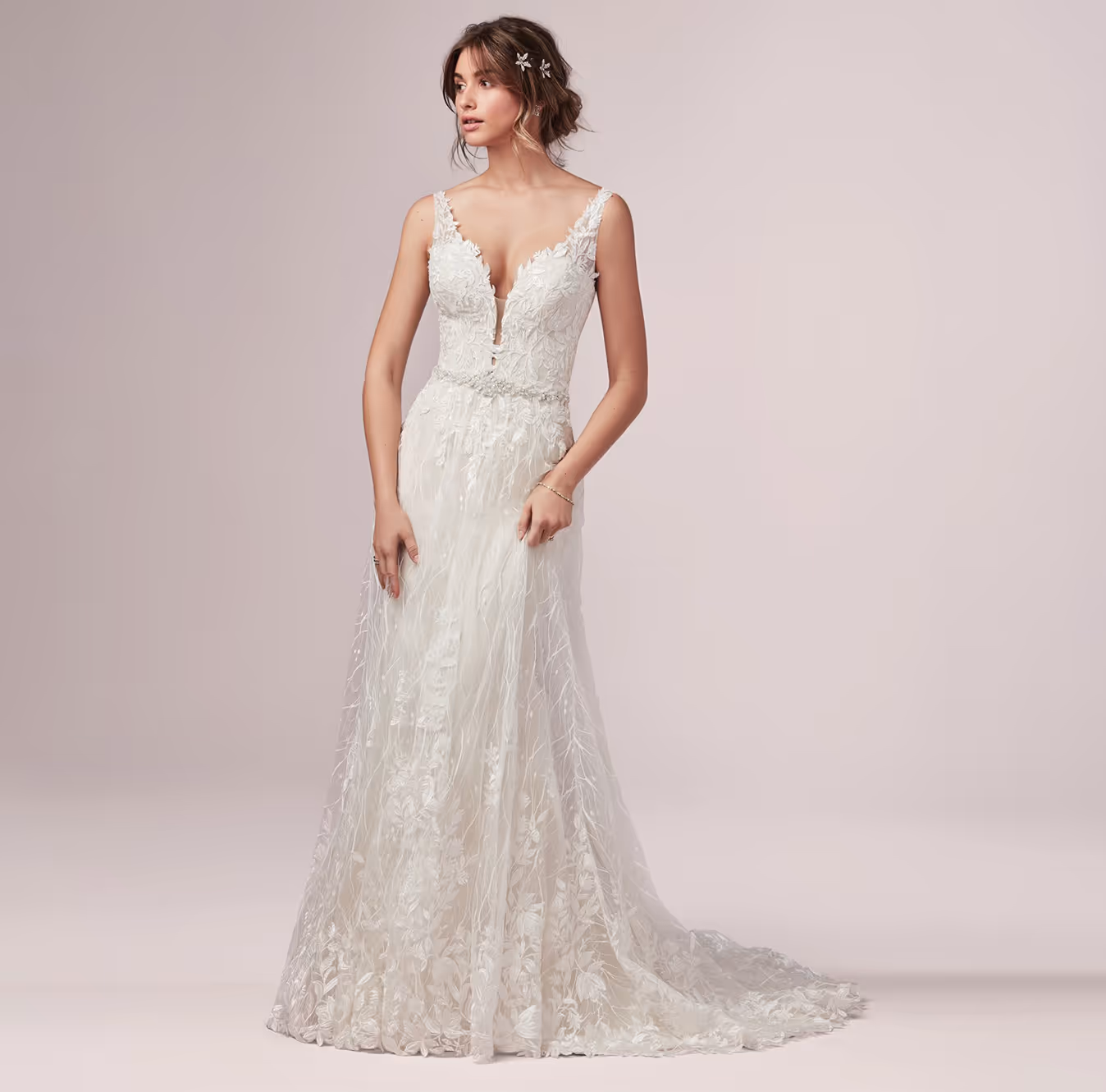 Woman in an elegant sleeveless white wedding dress with lace and floral embroidery, standing against a plain light background.