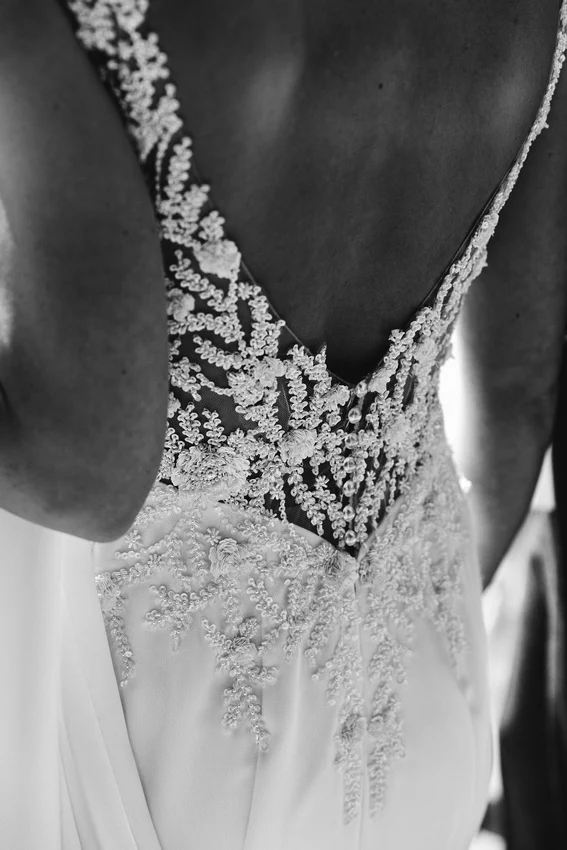 Close-up of a bride's back showing intricate lace and bead details on a sleeveless wedding dress with a deep V-cut.