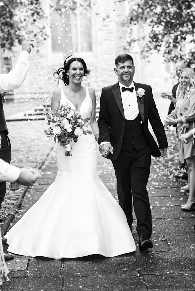 Bride and groom holding hands and smiling as guests throw confetti during their wedding celebration.