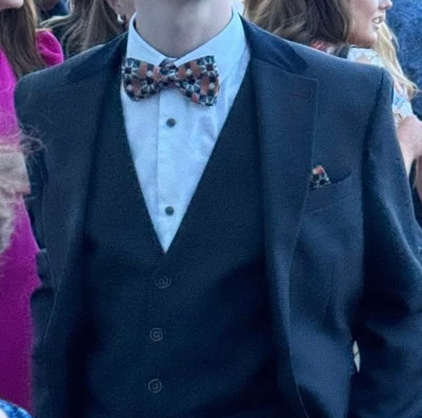 Man wearing a dark suit with a vest, a light blue dress shirt, and a checkered bow tie matching a pocket square.