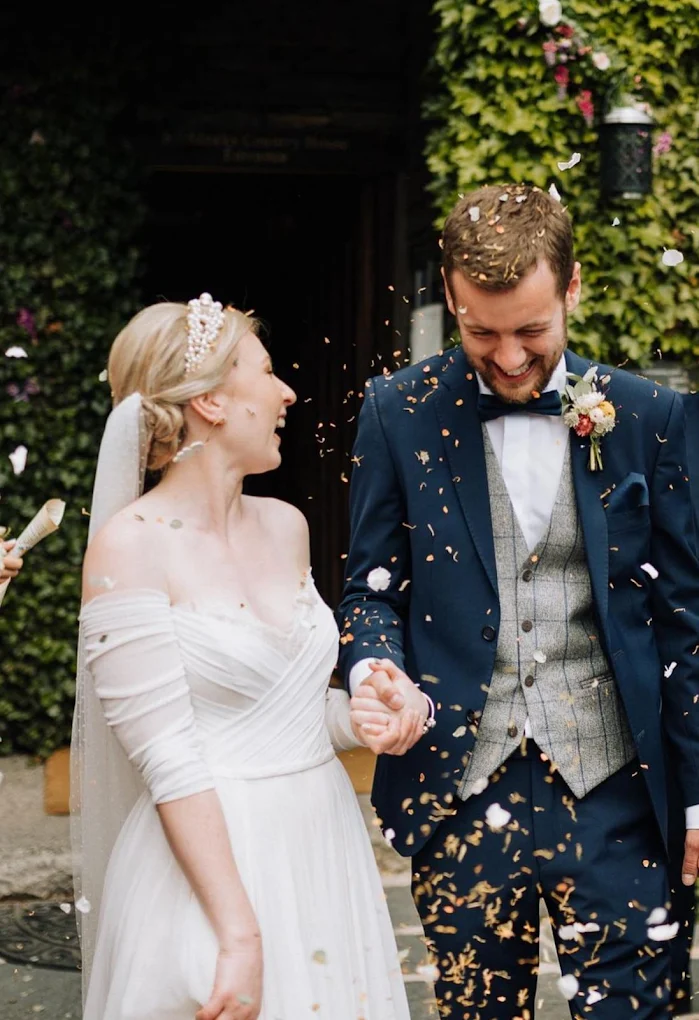 Bride and groom holding hands and smiling as flower petals are thrown during their wedding celebration.