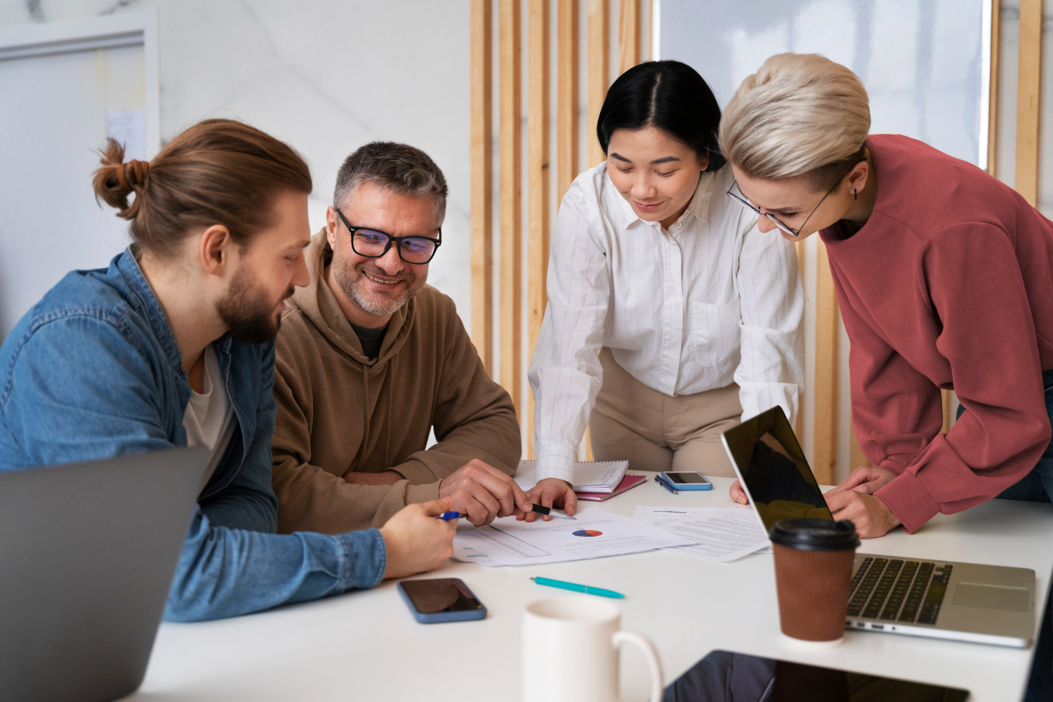 Four colleagues gathered around a table, discussing documents and laptops during a meeting.
