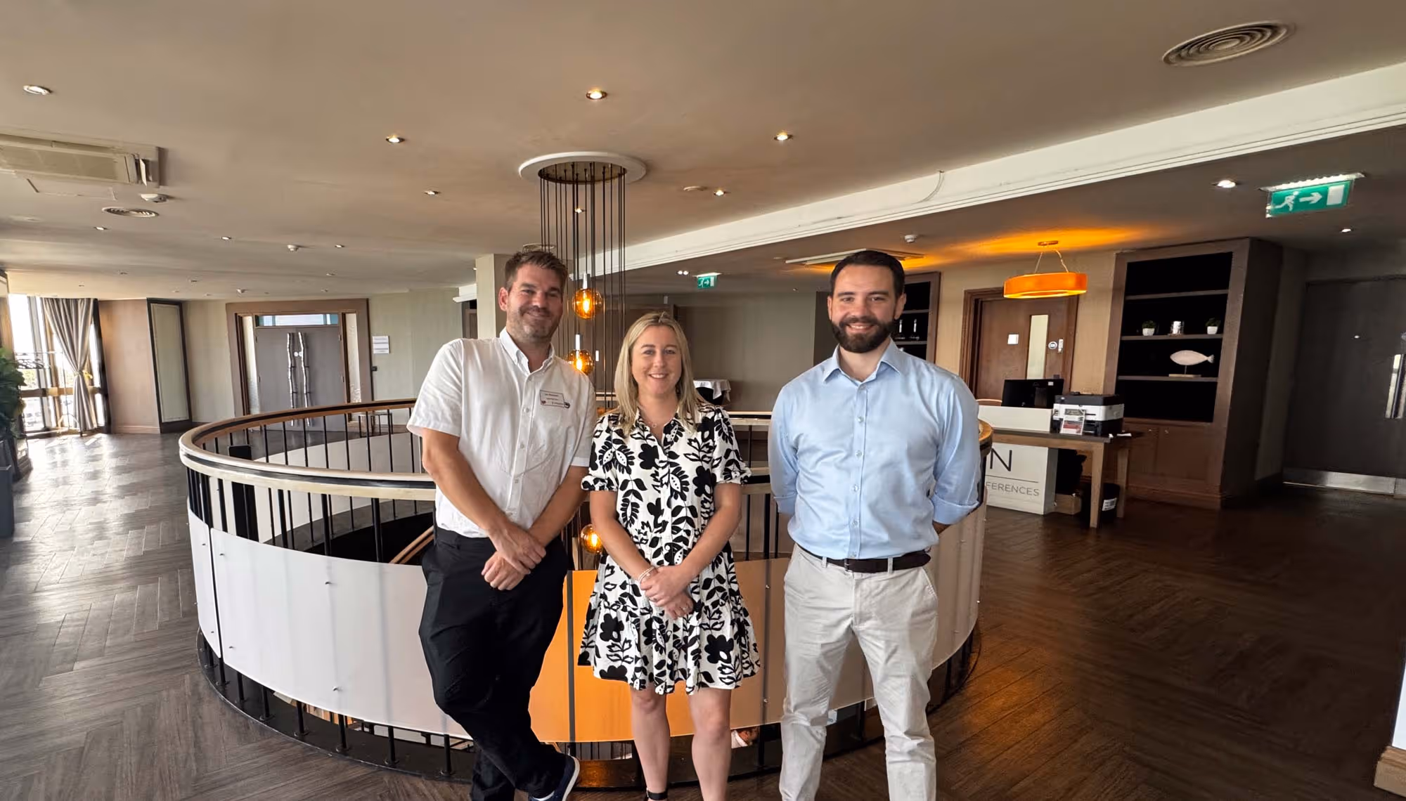 3 people stood in the lobby of a hotel in front of the top of a spiral staircase