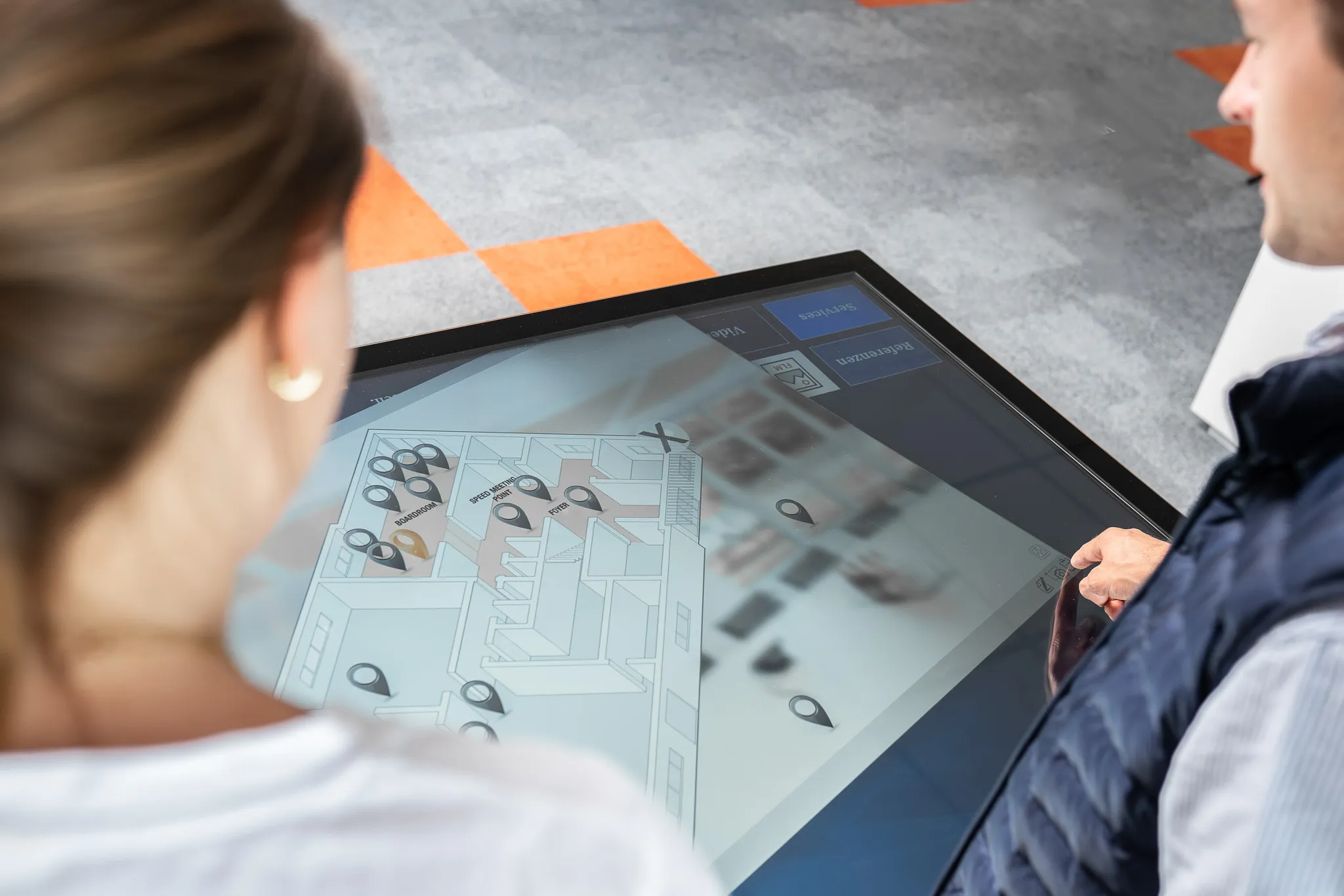 Zwei Personen, die an einem interaktiven Touchtisch ein Besucherleitsystem bedienen.