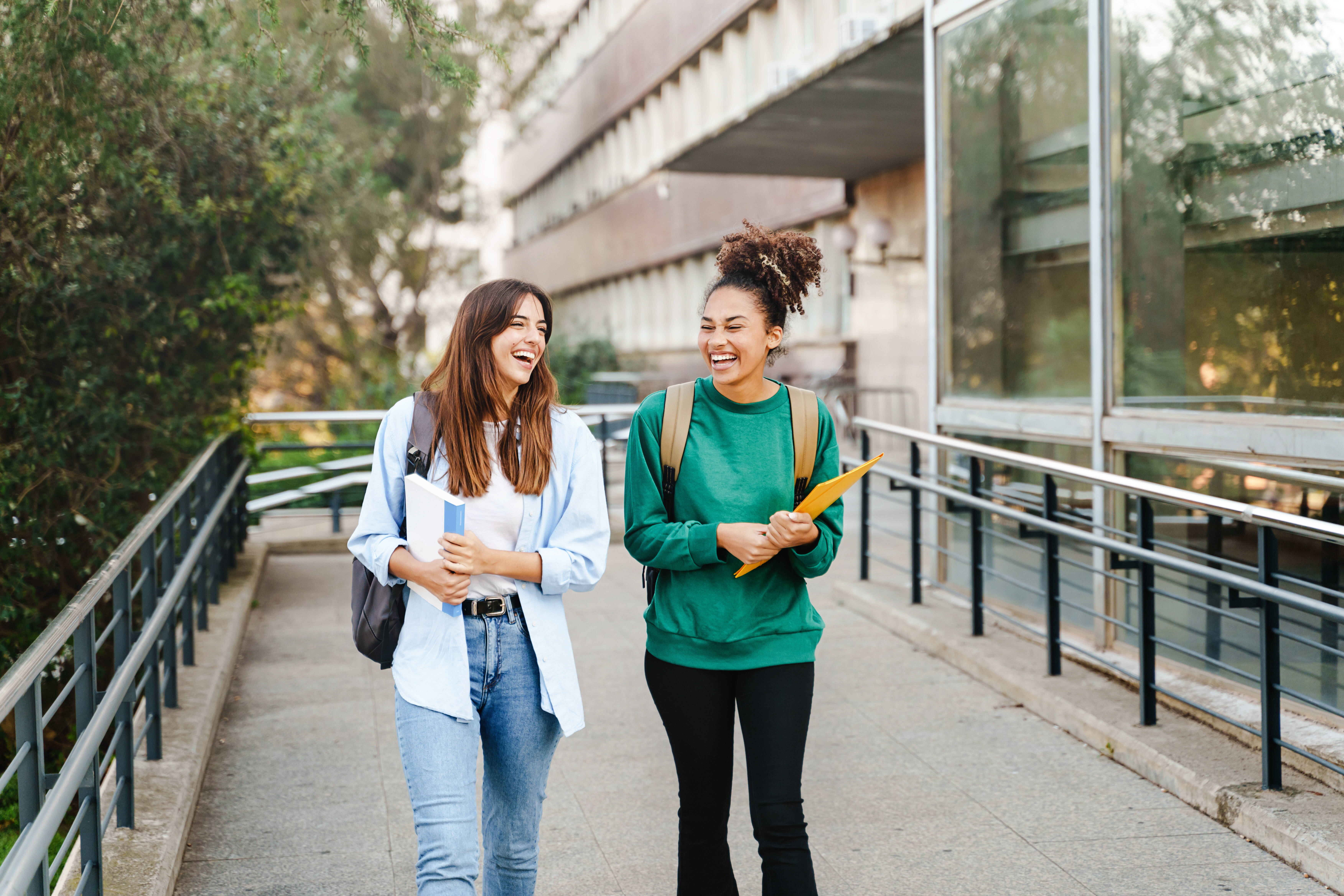 two laughing students leaving class with folders in hand