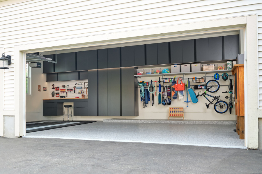 Modern organized garage with custom black storage cabinets, wall-mounted bike storage, slatwall organization system, and epoxy-coated flooring in a residential home garage.