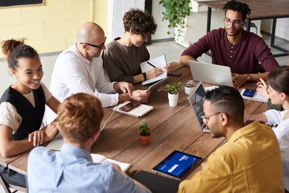 A team of professionals engaged in a virtual meeting, some smiling while others are taking notes, symbolizing collaboration despite interruptions.