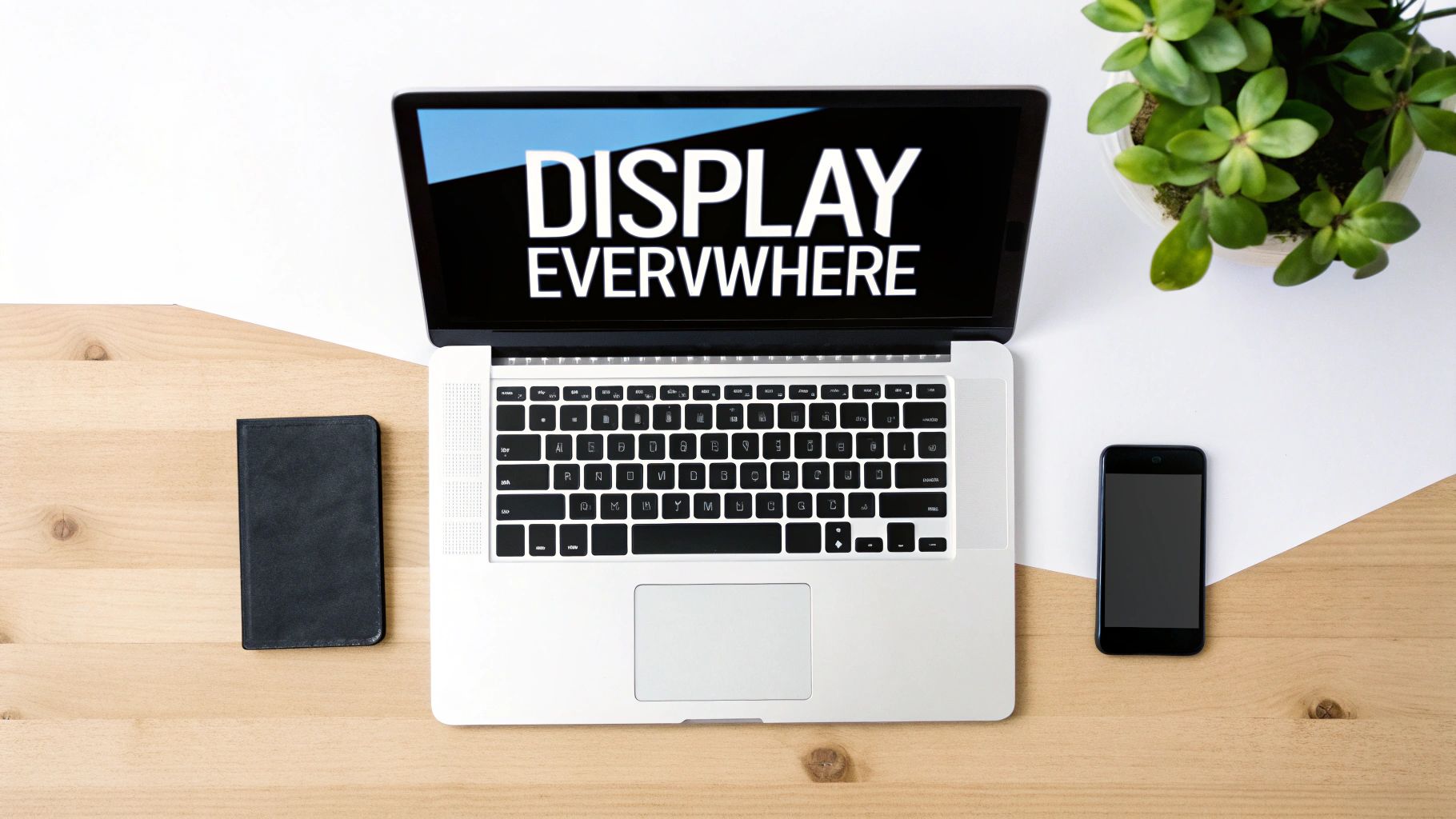 A top-down view of a laptop displaying 'DISPLAY EVERYWHERE', a phone, and a notebook on a modern workspace.