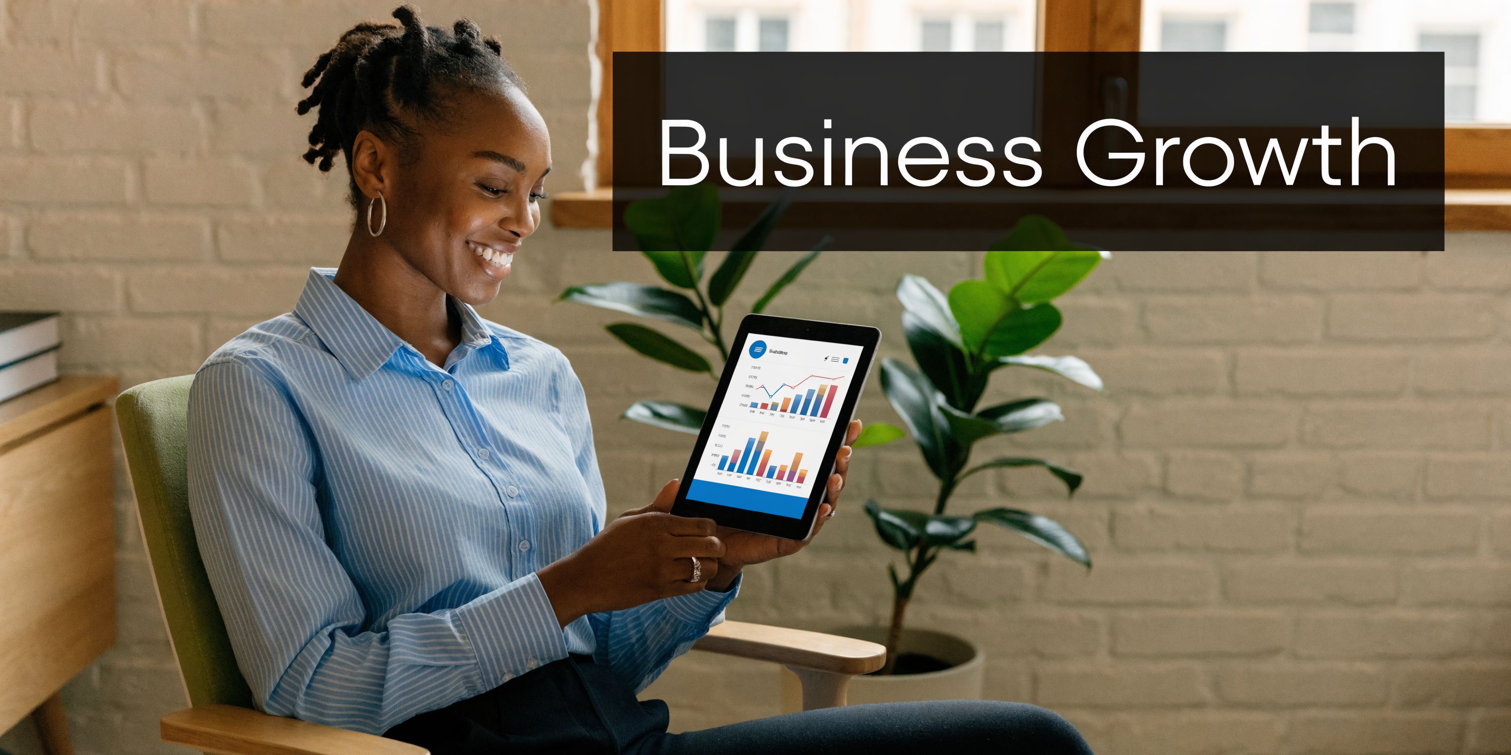 A professional woman sitting in a chair holding a digital tablet displaying business statistics and growth charts.
