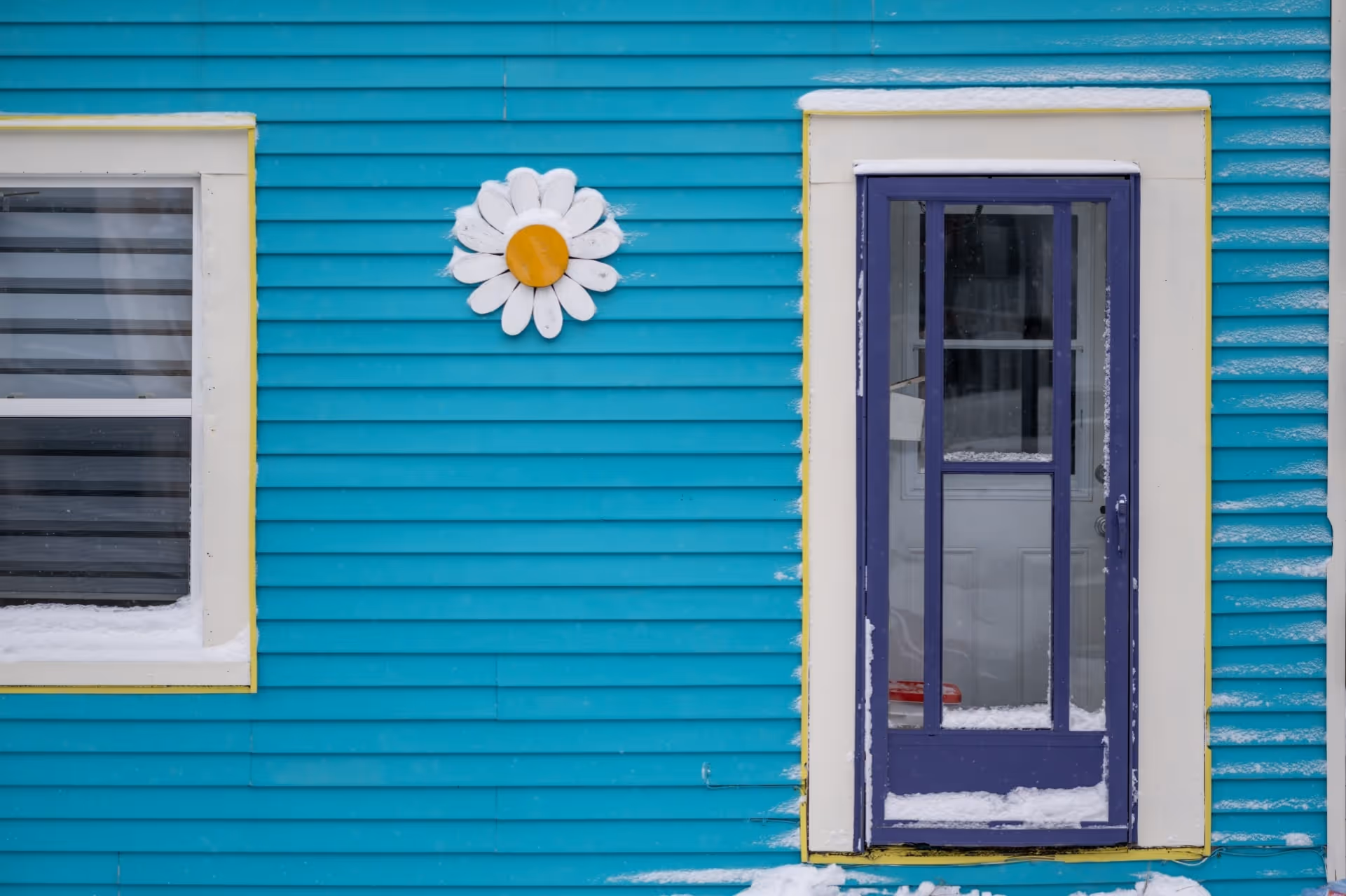 A home with teal siding and a snow-covered blue mid-view storm door with grid panels 