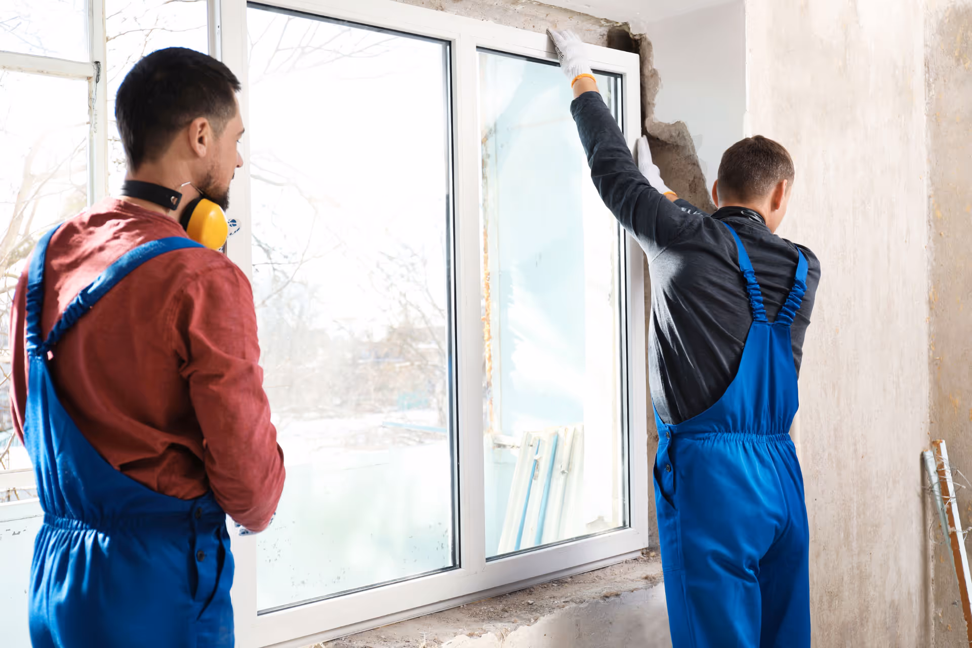 Two window professionals wearing blue overalls installing picture windows