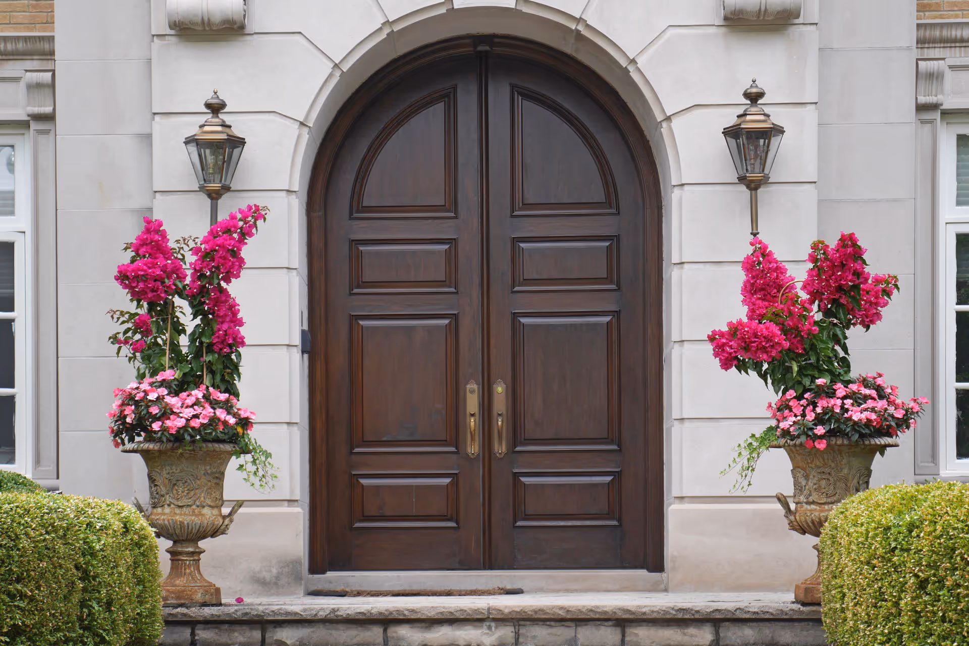 Front entrance with arched double front doors and pink flowers on either side of the entry doors