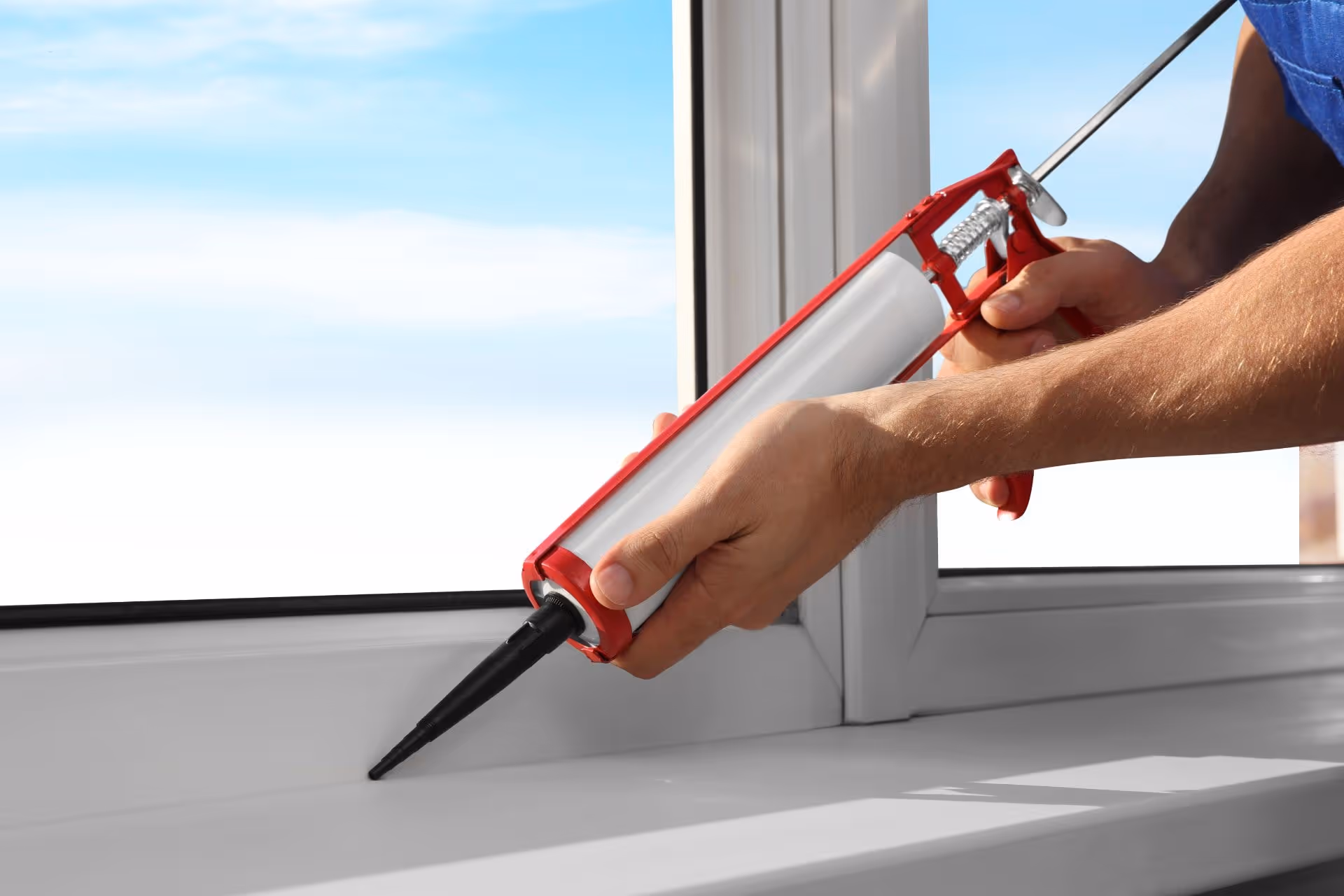A person applying window caulking on a window sill