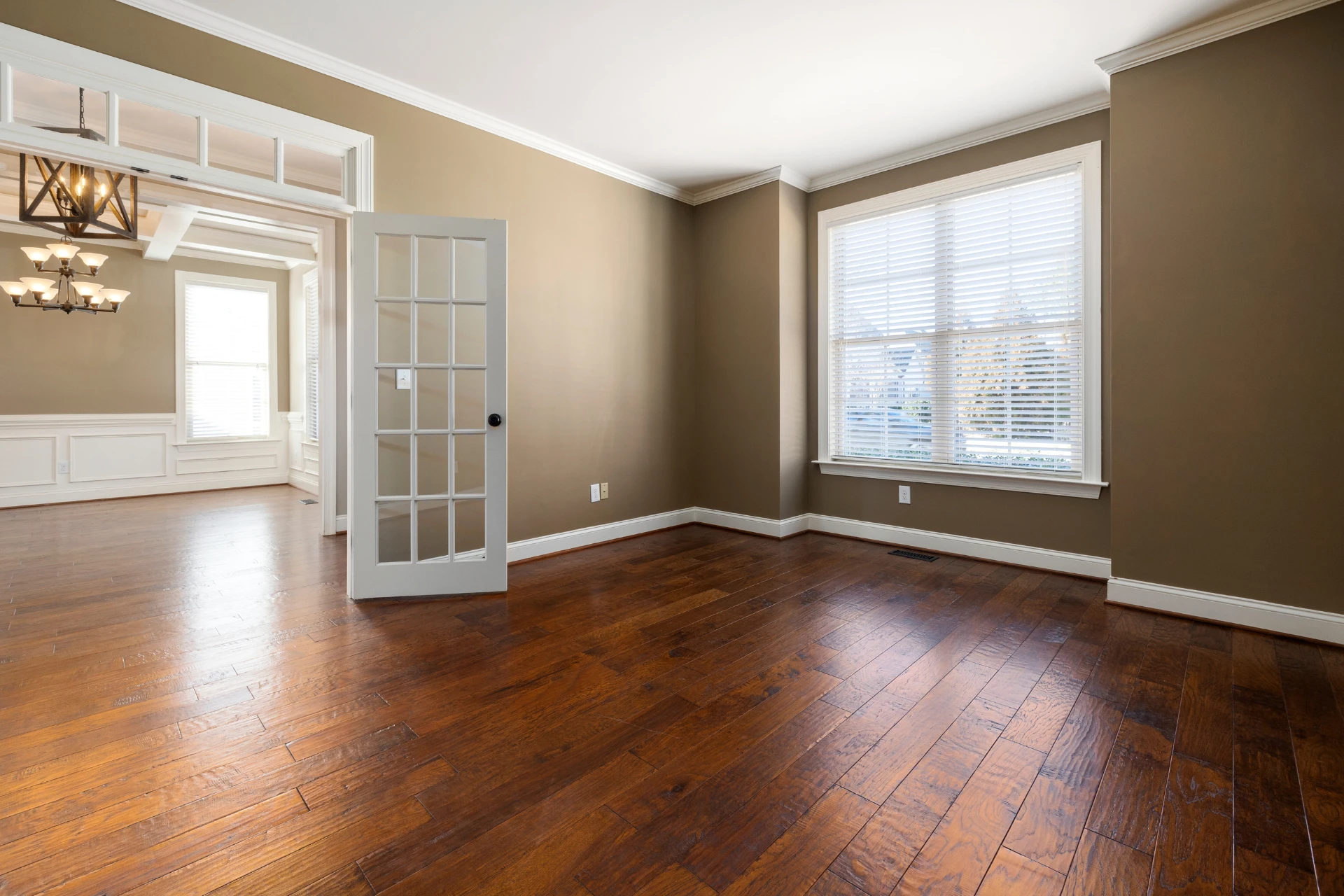 A bare rental house with polished wooden floors and double-hung windows covered by blinds
