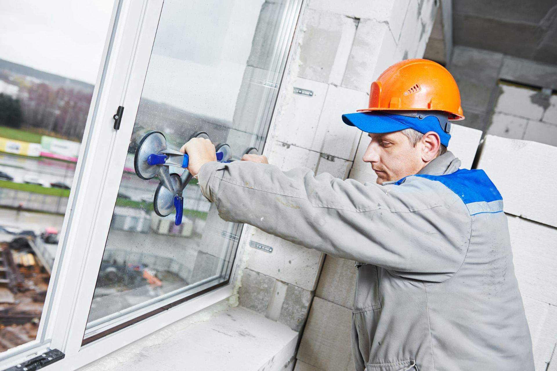 A window technician installs a glass window pane using a commercial-grade glass suction lifter