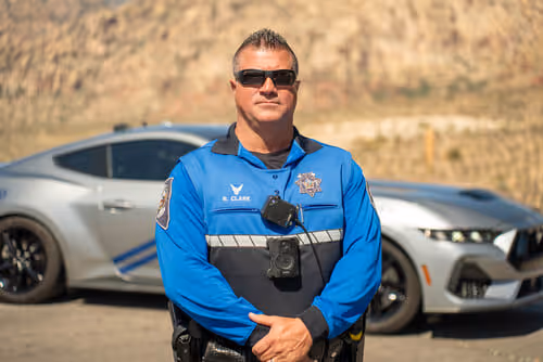 male officer in blue uniform in front of car