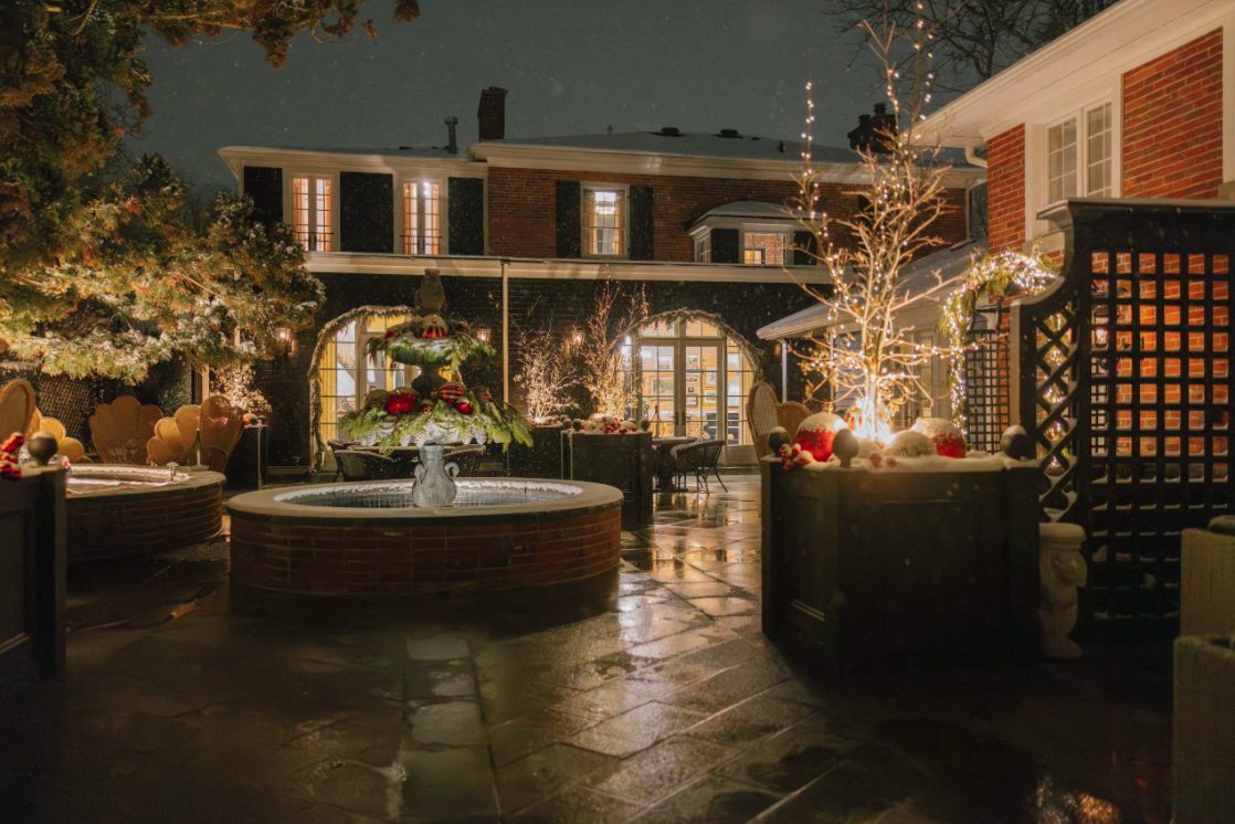 Snow-dusted courtyard at The Scotsman Hotel at night, with a decorated fountain, string lights, and holiday greenery