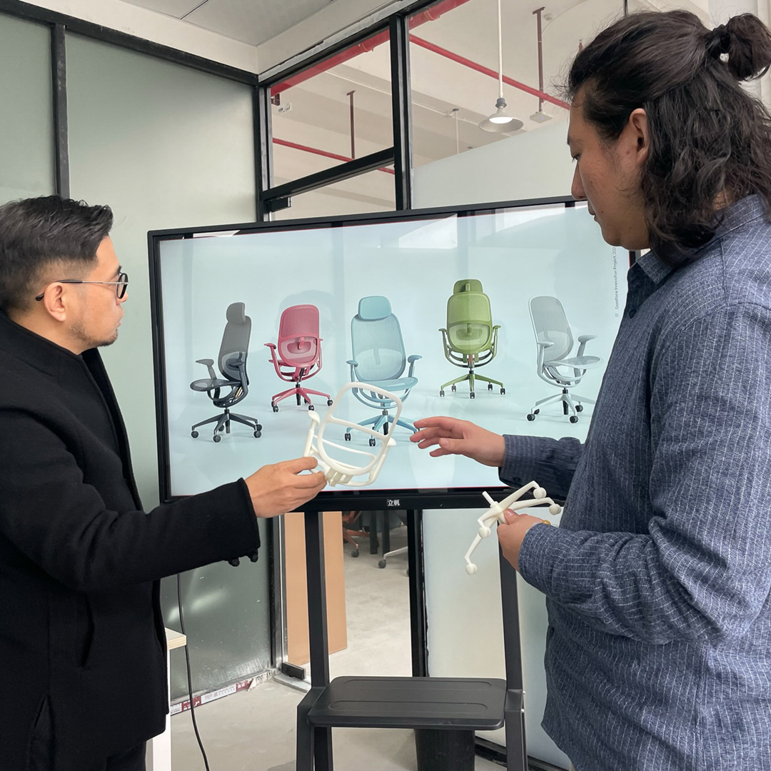 A designer explaining an idea to a client in from of a TV screen showing a concept rendering of the design.