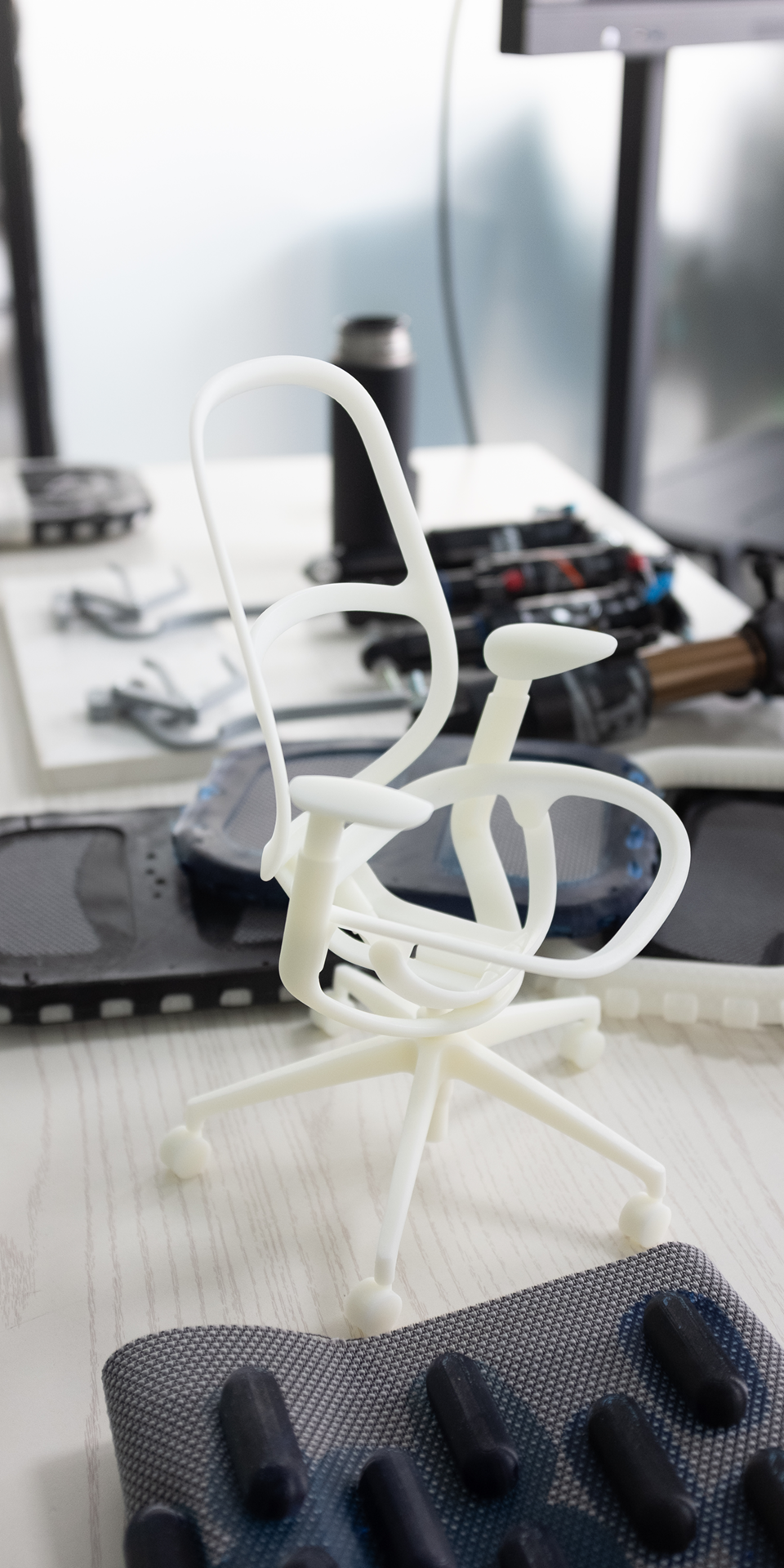 A white 3D printed scale model of the O2 chair on a table alongside other prototypes and material samples.