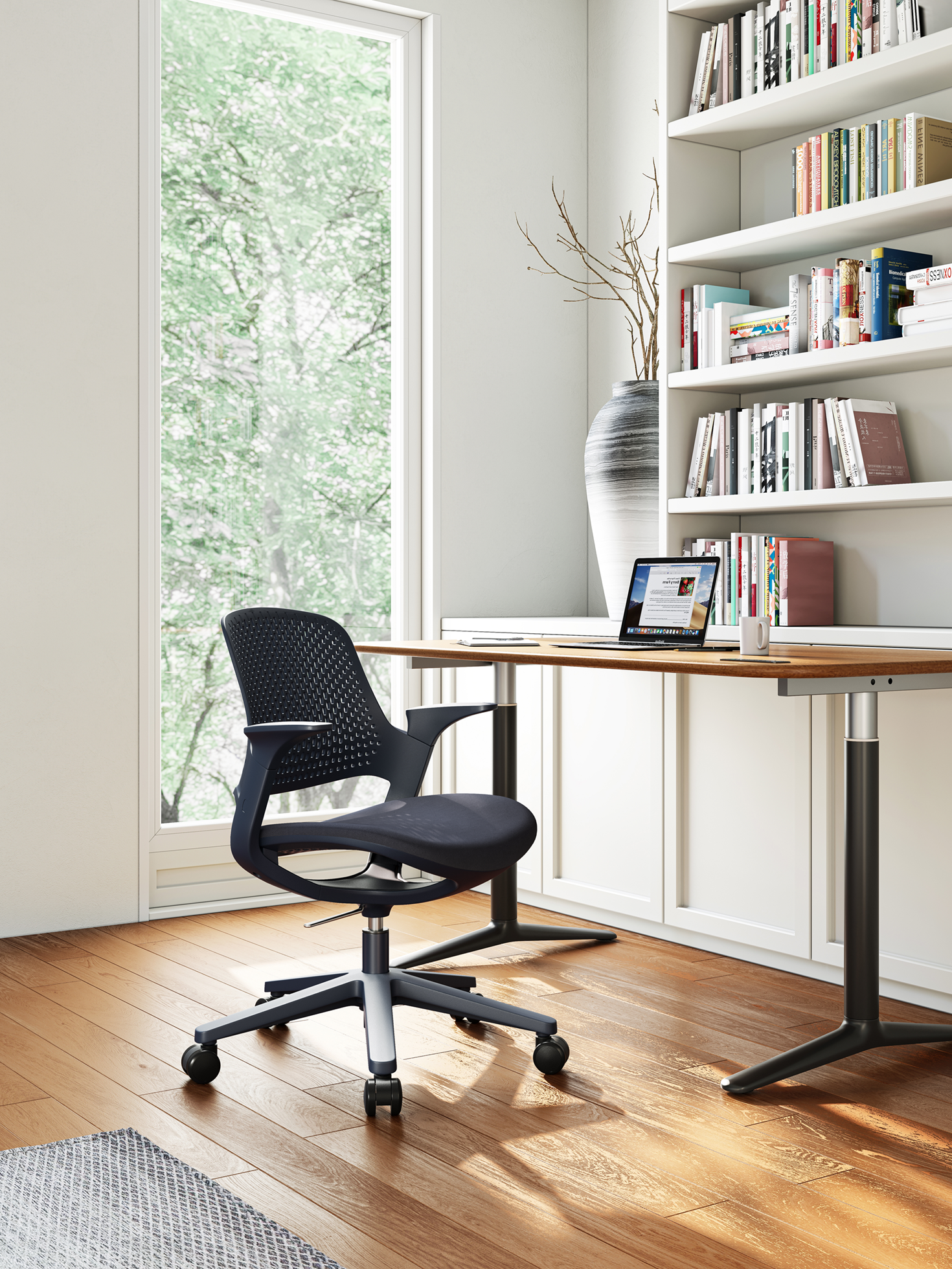 Modern home office with a black ergonomic office chair on wheels, wooden floor, large window showing green trees, white desk with a laptop and coffee mug, and built-in bookshelves filled with books and a tall decorative vase with branches.