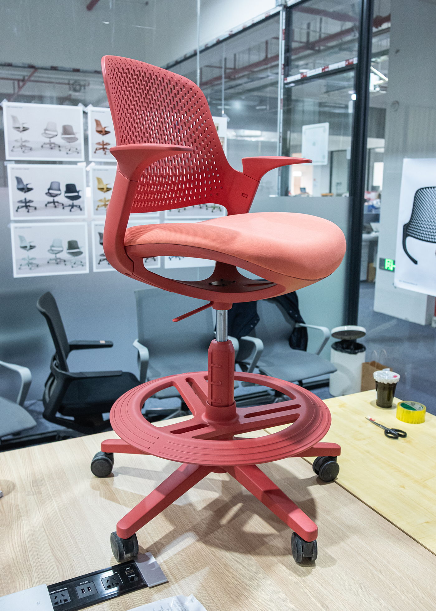Red ergonomic office chair prototype with mesh back and padded seat on caster wheels placed on a wooden table.