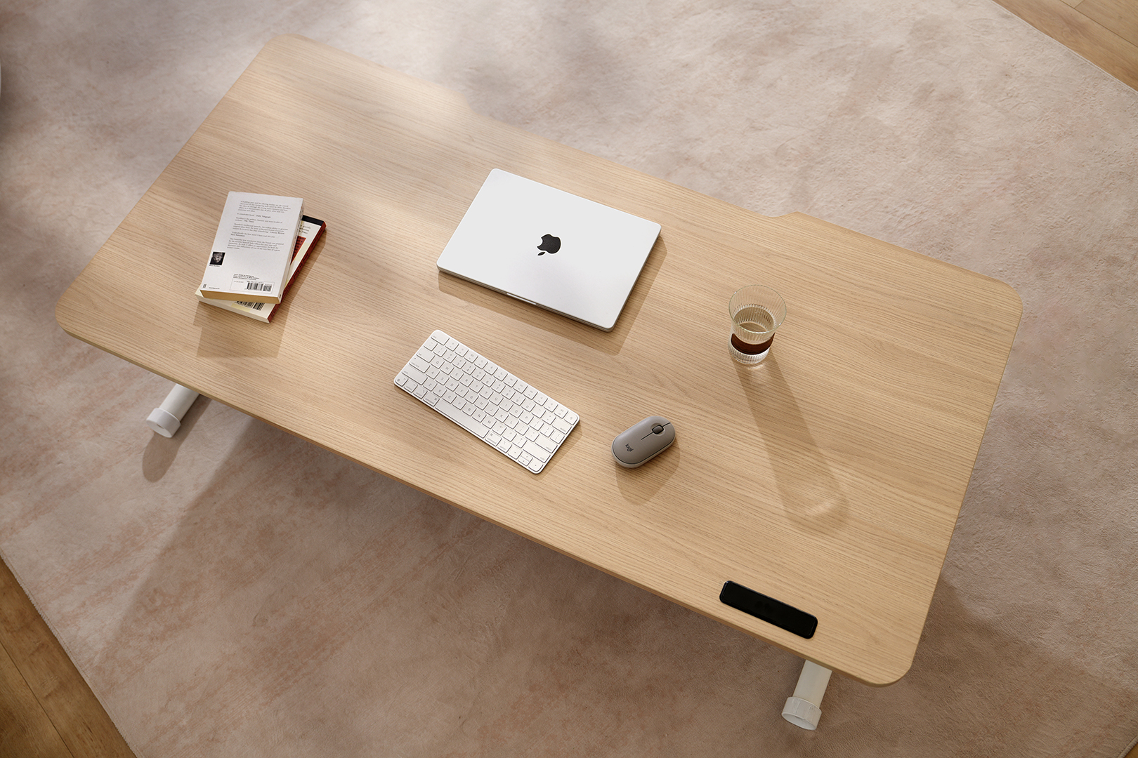 Top 3/4 view of the marina mantra flow desk showing an oak laminate work top with a laptop, mouse, water glass and book on the surface.